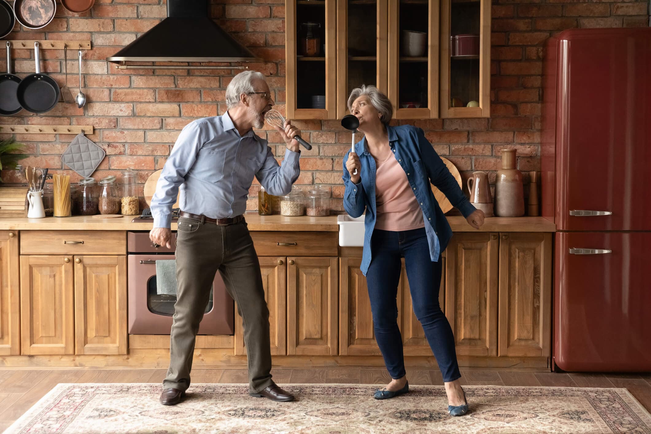 Dos adultos mayores disfrutando de un momento de calidad en sus vidas, jugando a cantar con utencilios de cocina y teniendo una buena comunicación entre ellos, tal como Kinexperience con sus pacientes
