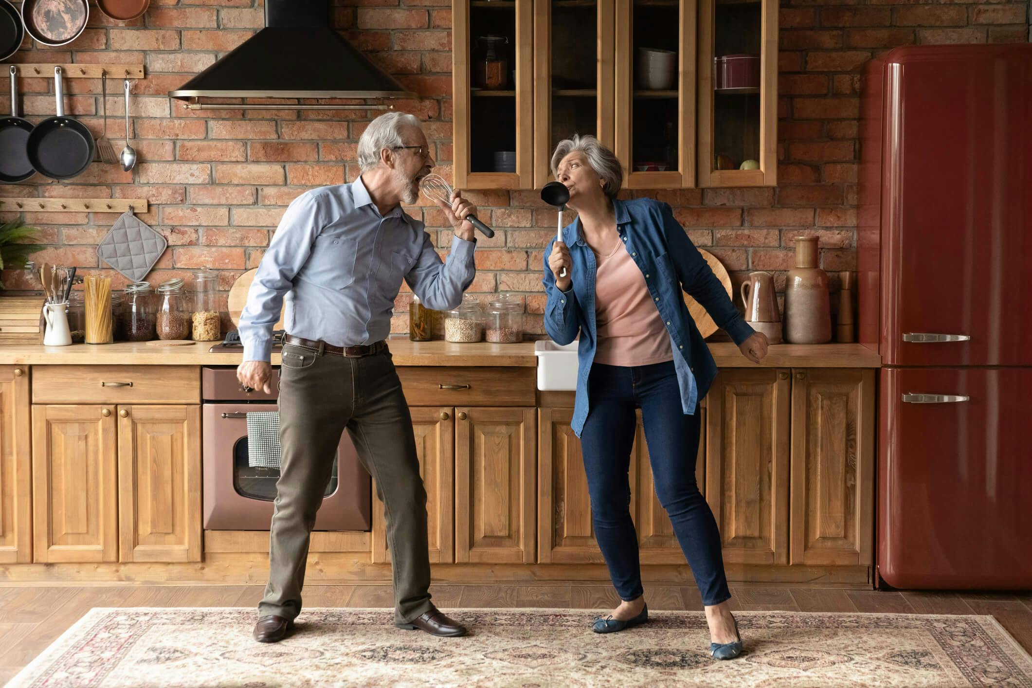 Dos adultos mayores disfrutando de un momento de calidad en sus vidas, jugando a cantar con utencilios de cocina y teniendo una buena comunicación entre ellos, tal como Kinexperience con sus pacientes